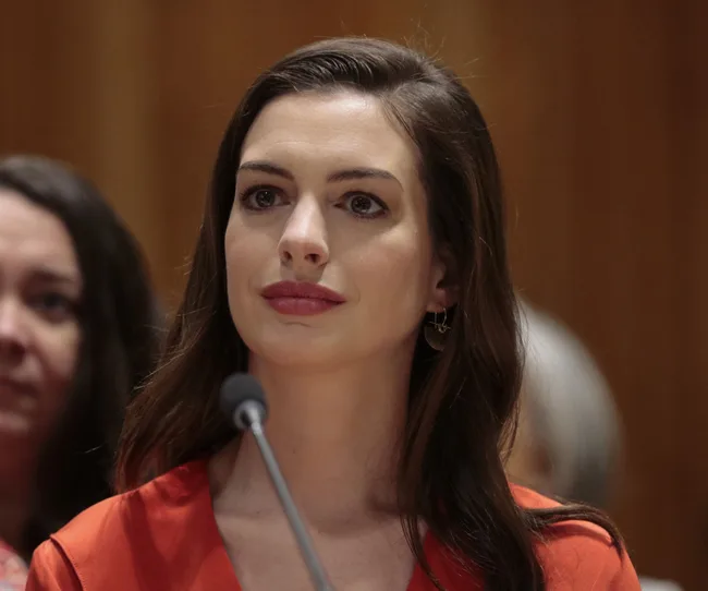 A person in a red outfit speaks into a microphone at a public event indoors.