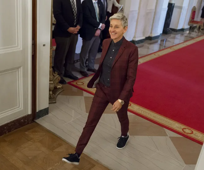 Person in a burgundy suit walking on a red carpet in a formal setting.