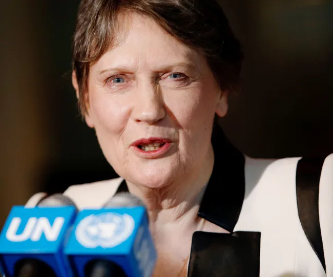 A woman speaks at a UN press conference, facing microphones with the UN logo.