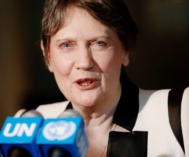 A woman speaks at a UN press conference, facing microphones with the UN logo.