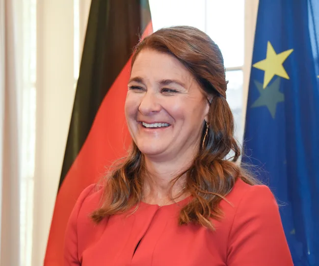 A woman in a red dress smiling in front of a German and European Union flag.