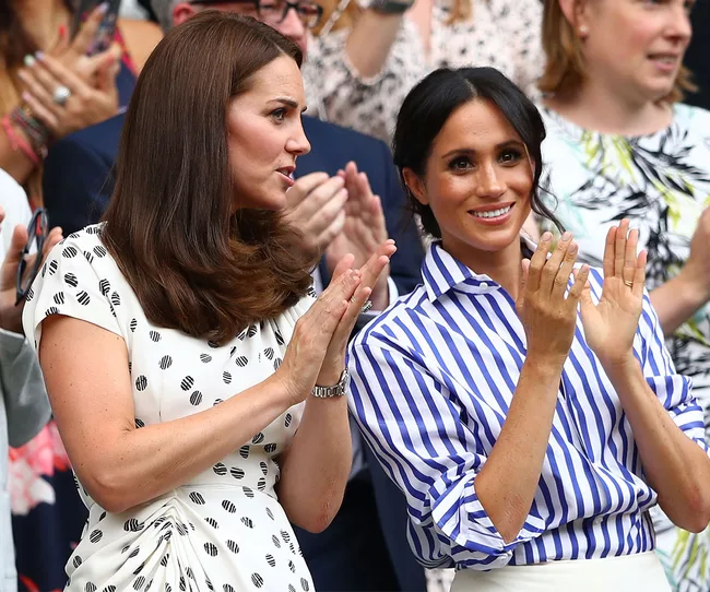 Two women in patterned dresses clapping at an event, surrounded by a crowd.