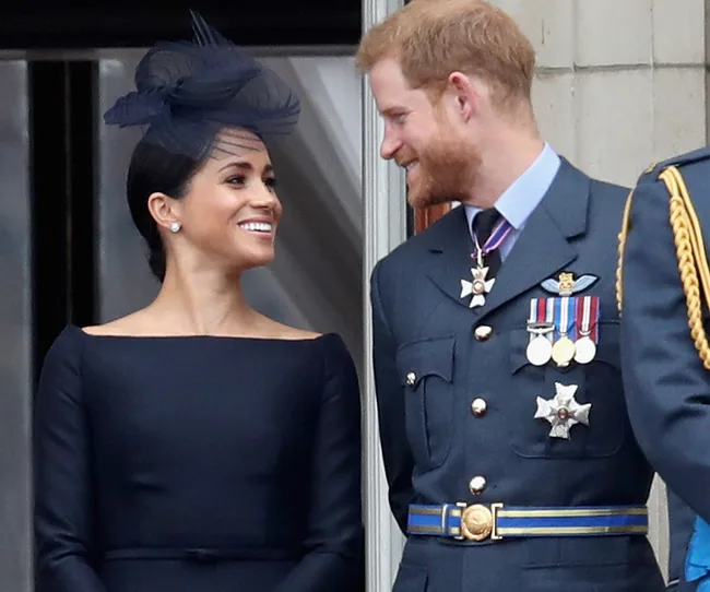 A man in a military uniform and a woman in a hat smile at each other, standing on a balcony.