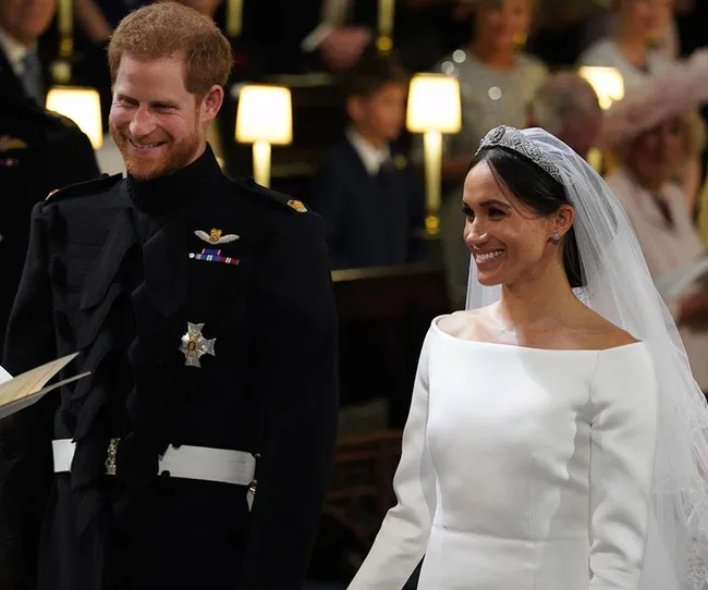 A smiling bride in a white dress and veil stands beside a groom in a black uniform during a formal ceremony.