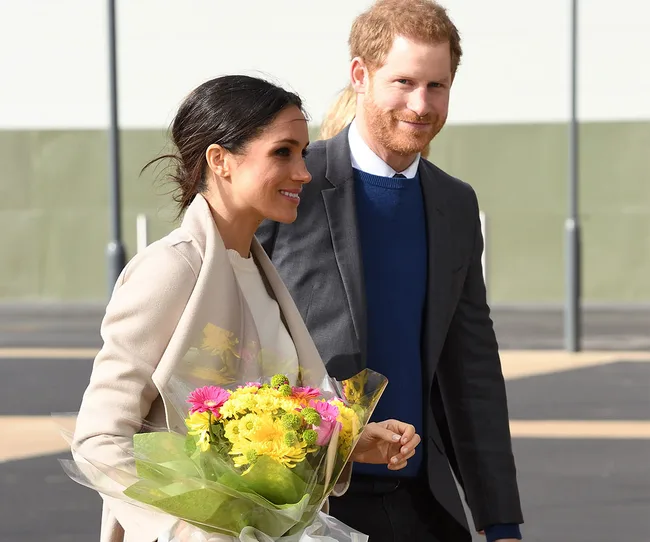 A woman holds a bouquet of colorful flowers while walking with a man in a suit, both smiling warmly.