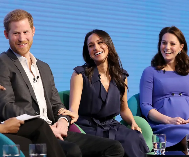 Three people sitting and smiling on a panel discussion, each holding microphones, with a blue background.