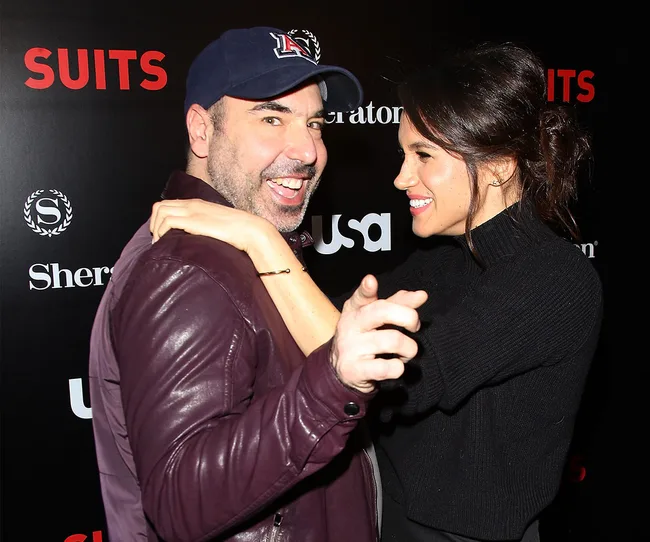 Two people smiling and posing at a "Suits" TV show event, with promotional logos in the background.