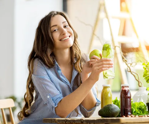 Happy woman sits at table with green vegetables and juices