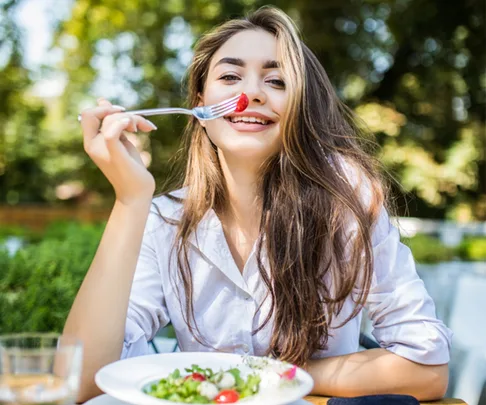 Happy young woman eats a salad in the sun
