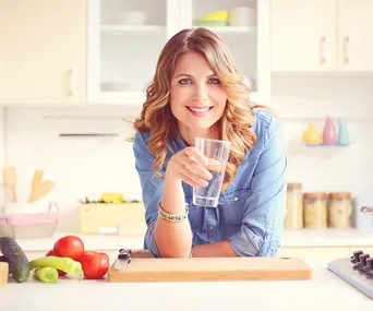 Woman smiling holding water in kitchen 