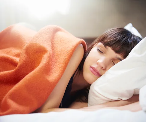 brunette woman sleeping with orange blanket