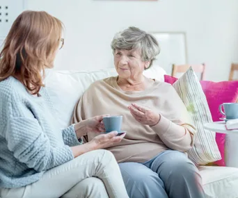 Elderly mother and adult daughter talk on couch