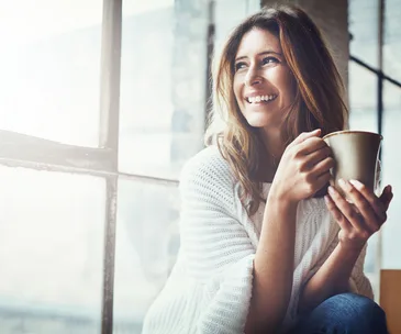woman smiling and looking out window while drinking tea