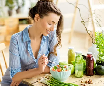 woman eating a salad surrounded by green vegetables on her table