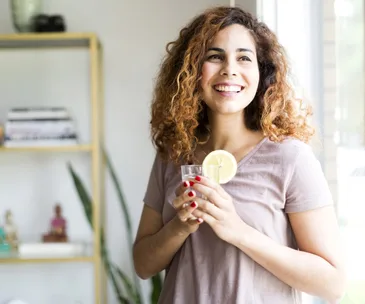 happy woman stands near window holding lemon water