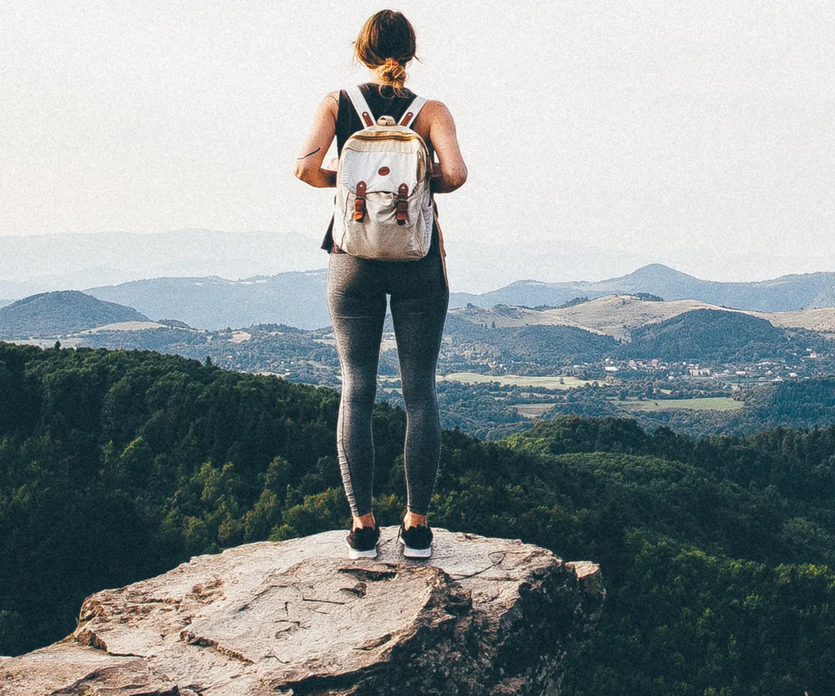 Casual female hiker looking out from summit over forest
