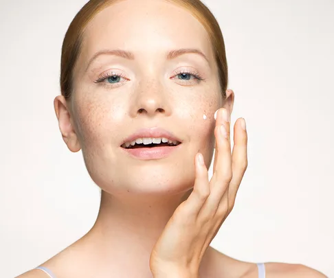 Blonde woman rubbing moisturiser into cheeks