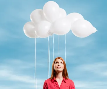 Red-headed woman looking up to sky white balloons forming clouds