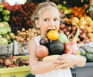 Young girl in market, arms full of produce
