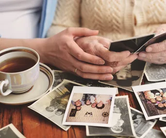 Senior woman and granddaughter sitting at table, looking through old photographs, mid section