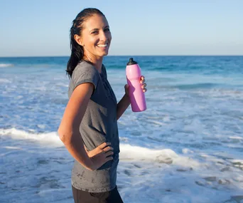 woman drinking from water bottle after exercise by the sea