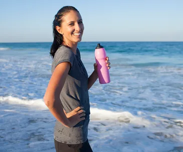 woman drinking from water bottle after exercise by the sea