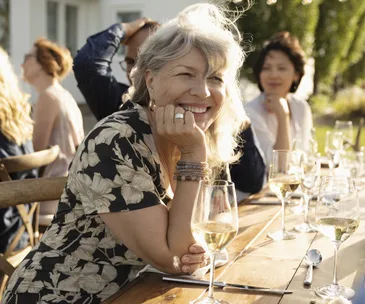 Smiling woman drinking wine at sunny garden party 