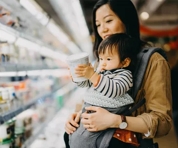 baby holding yoghurt tub in supermarket with mum