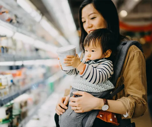 baby holding yoghurt tub in supermarket with mum