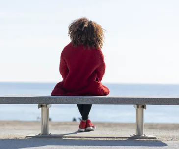 Rear view young woman sitting on a bench looking to horizon over sea
