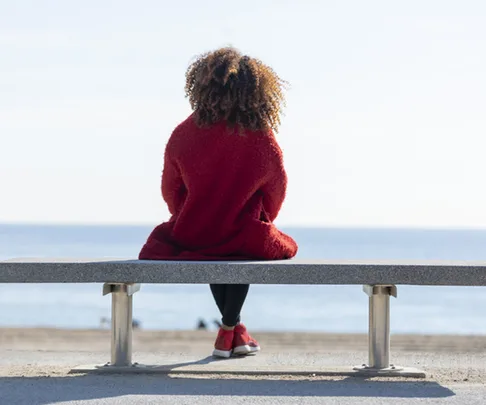 Rear view young woman sitting on a bench looking to horizon over sea