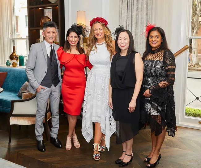 Group of five people posing indoors, wearing formal attire and decorative headpieces, with a stylish interior backdrop.