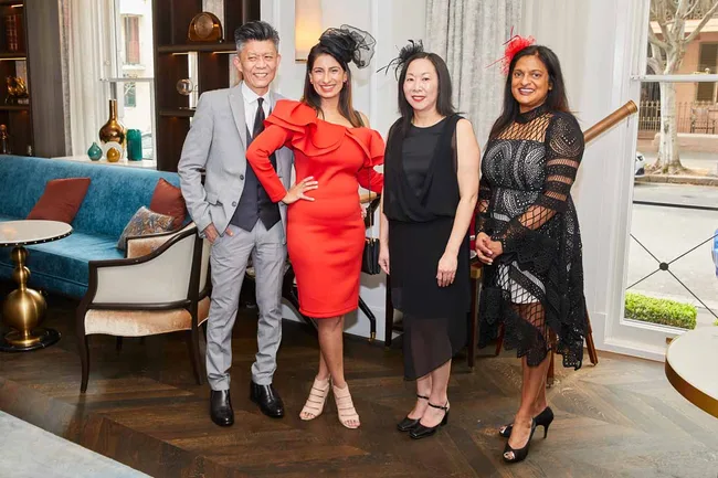 Group of four people dressed formally, standing indoors, smiling at the camera.