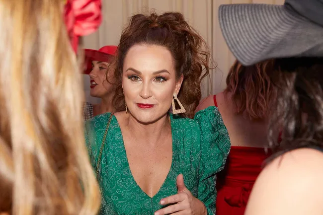 Woman in a green dress with triangle earrings at a social event, surrounded by others in hats and vibrant attire.