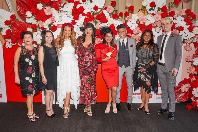 Group of people posing in front of a floral red and white backdrop at a Colgate Optic White event.