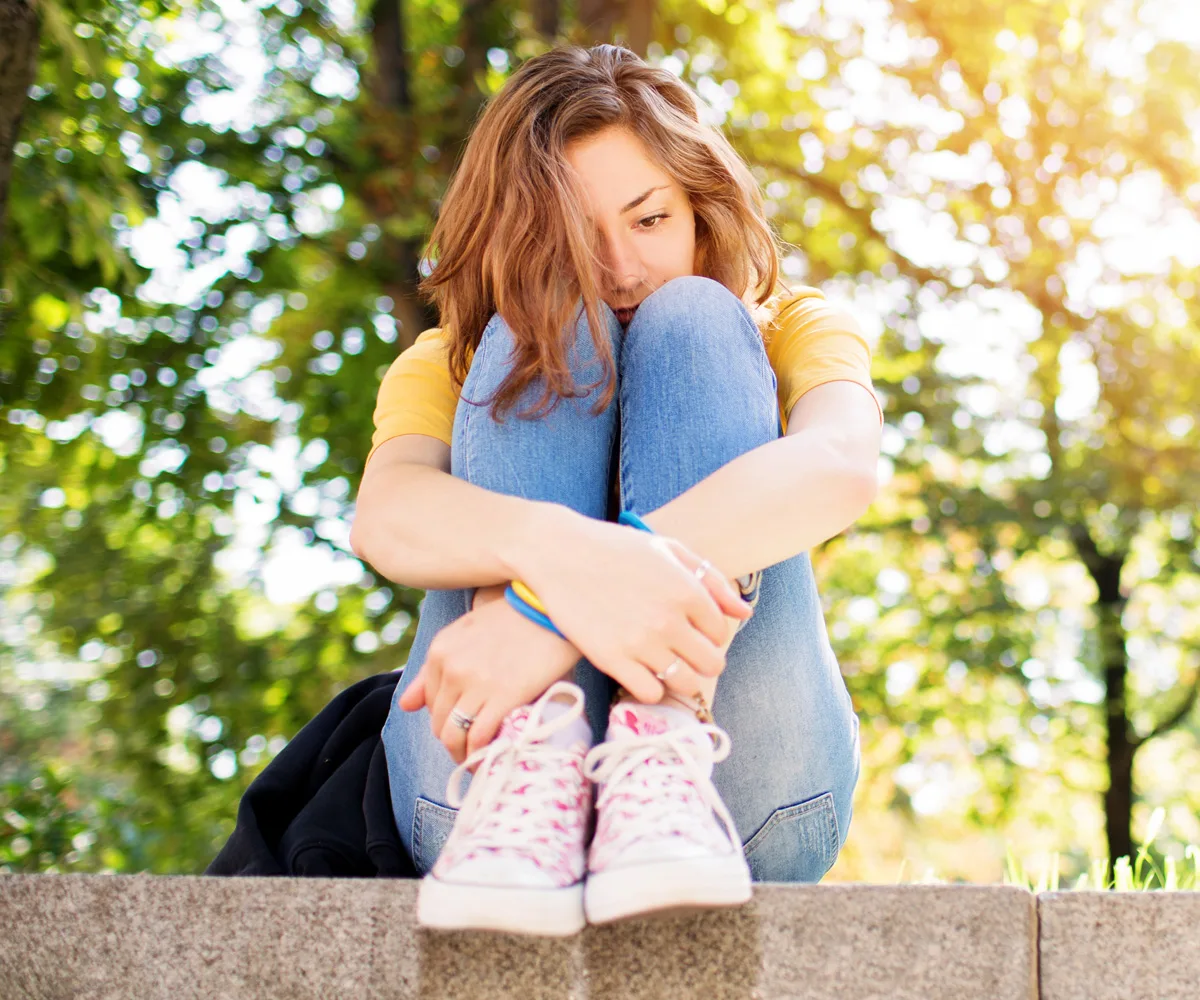 Sad teen sitting on wall hugging knees