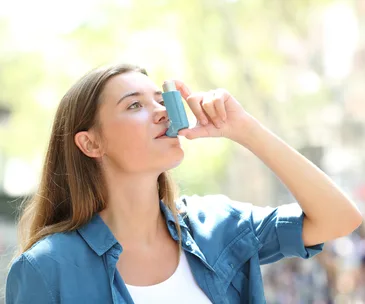 Asthmatic woman using inhaler standing in the street