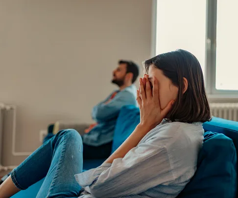 frustrated woman sits on couch, boyfriend background