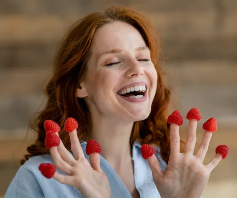 laughing redheaded woman with raspberries on her fingertips