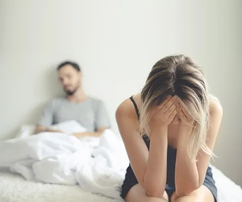 Woman sits on end of bed, head in hands