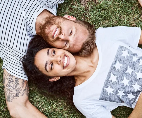 Multi-ethnic couple lying on grass at back yard