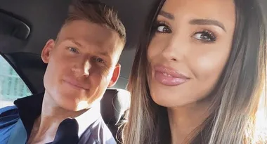 A man and woman smiling together in a car, with sunlight illuminating their faces from outside.