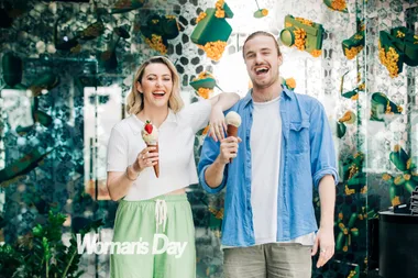 Two people smiling, holding ice cream cones with a colorful backdrop, Woman's Day text visible.