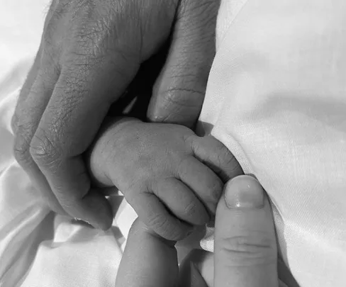 Adult and baby hands gently holding each other, showing tenderness and connection. Black and white photograph.