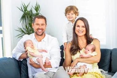Family with two adults, toddler, and twins sitting on a couch, smiling. New Zealand Woman's Weekly logo in corner.
