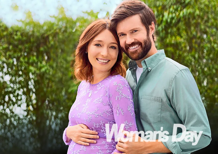 Couple smiling, woman in a purple dress, man in a light green shirt; outdoors with greenery, "Woman's Day" logo present.