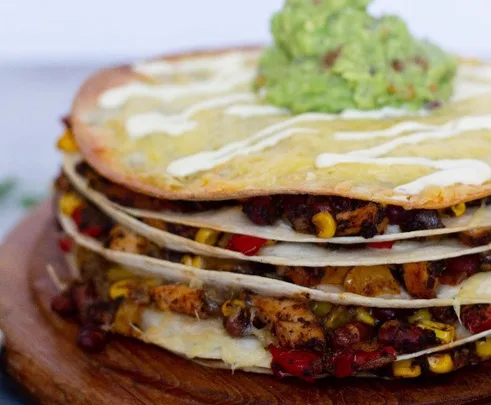 Layered Mexican tortilla stew topped with guacamole, featuring chicken, peppers, corn, and melted cheese.