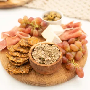 Charcuterie board with pâté, crackers, red grapes, cheese, cured meat, and olives on a wooden platter.