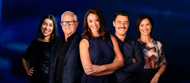 Five people standing together, smiling in front of a dark blue background, dressed in formal and semi-formal attire.