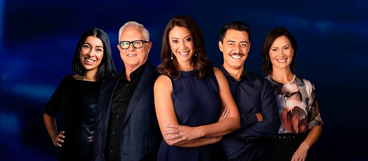 Five people standing together, smiling in front of a dark blue background, dressed in formal and semi-formal attire.